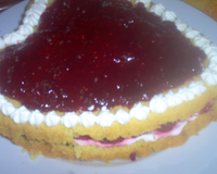 Gâteau en forme de coeur avec du coulis de framboises, des framboises et de la chantilly