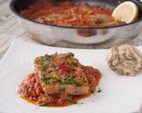 Dans un plat type paella, un lit de poivrons, oignons doux et tomates, le poisson cuit dessus, à couvert, et arrosé d"un filet de citron et parsemé de coriandre fraîche,…