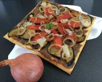C'est une fine pate feuilletée avec un confit d'oignons et anchois , agrémentée d'aubergines, pétales de tomates rondelles d'oignons roscoff, huile d'olive et copeaux…