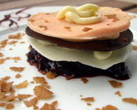 Dessert constitué de trois disque de chocolat noir, blanc et orangé avec un coulis fruits rouges.