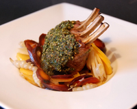 Un carreau d'agneau en croûte d'herbes sur un lit de légumes racines oubliés