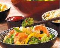 Des légumes tendres, des queues de crevettes et des nouilles chinoises revenus dans l'huile d'olive avec de la sauce soja, à servir avec une sauce ketchup/soja.…