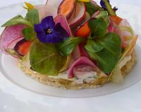 Il s'agit d'un disque de focaccia aux herbes surmonté de fromage frais avec des herbes fraîches et des légumes croquants disposés dessus.