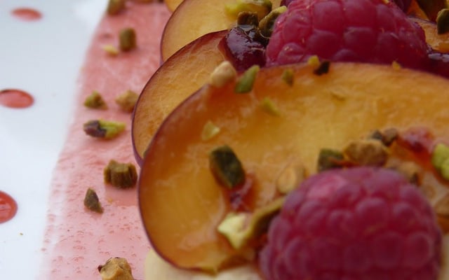 Tartines pêches-framboises parsemées de pistaches et de miel sur de la crème aux amandes